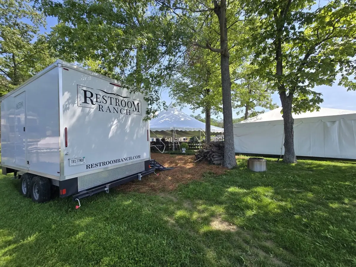 Restroom Ranch trailer parked among trees beside white event reception tents