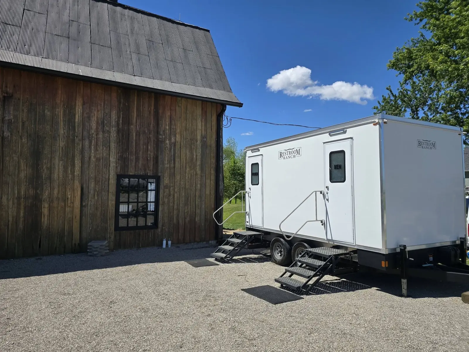 A branded Restroom Ranch luxury restroom trailer set up beside a rustic barn venue under a blue Indiana sky
