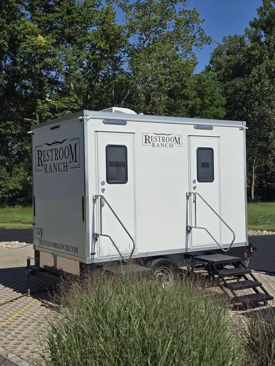 Branded Restroom Ranch 2-station trailer with women's and men's entrances beside ornamental grasses